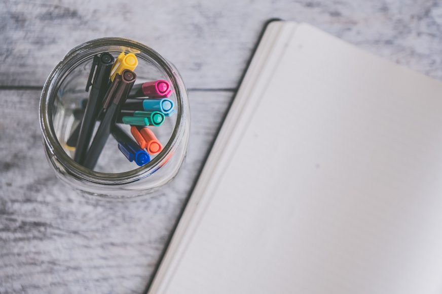 pot of pens next to blank notebook